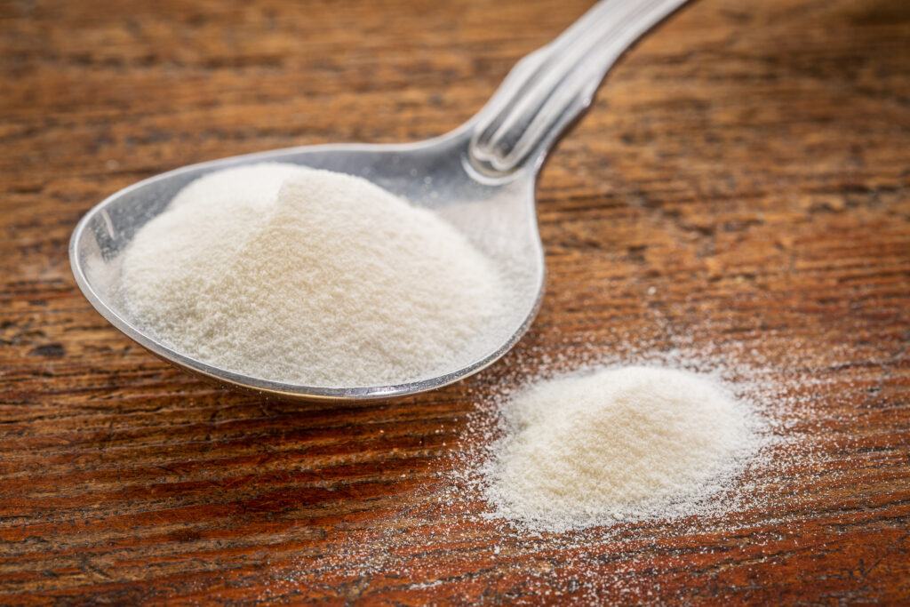 A spoonful of collagen powder on a wooden surface, with a small quantity spilled beside it.
