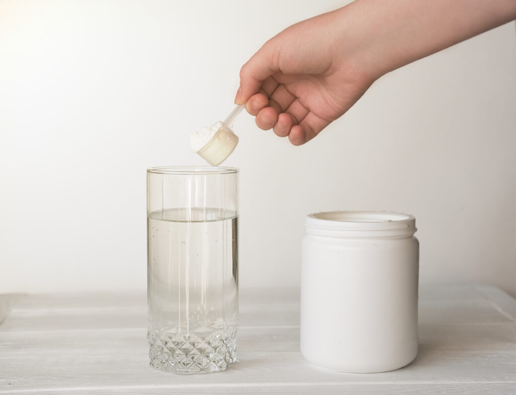 A hand scooping collagen powder into a glass of water.
