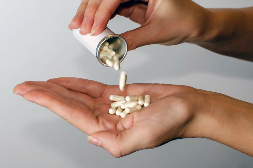 Probiotic capsules being poured from a bottle into an open hand.