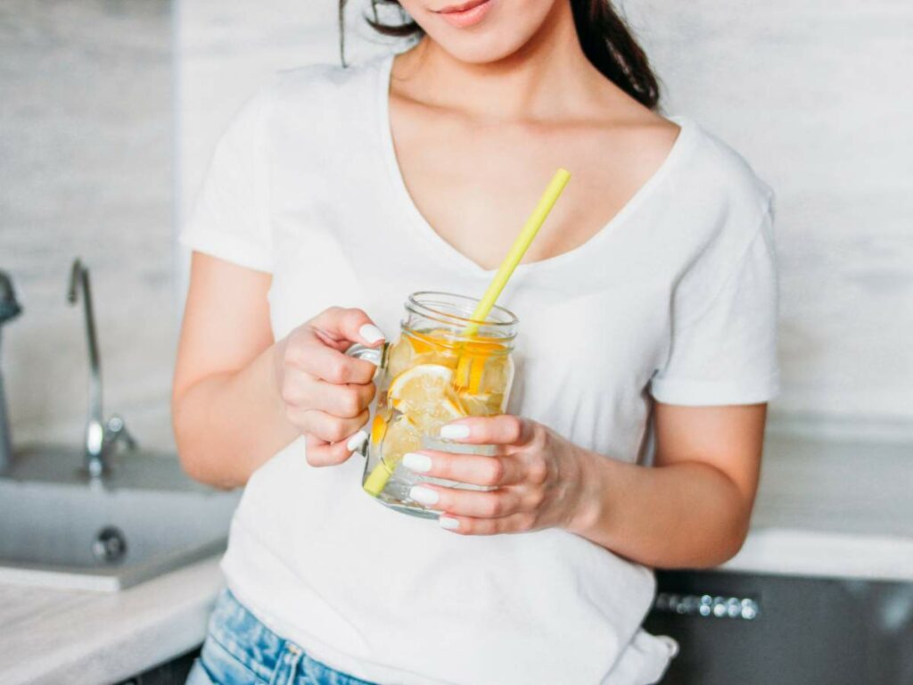 Woman holding a glass jar with lemon water and a straw.