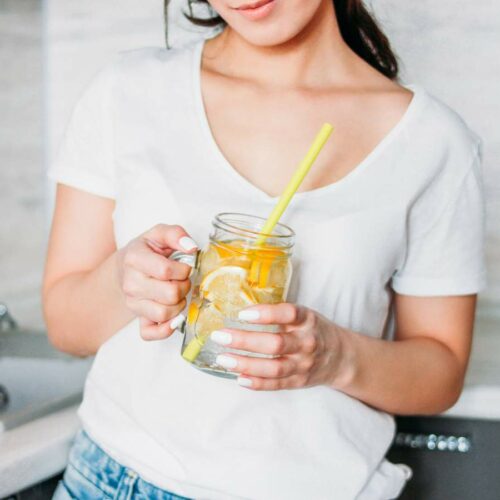 Woman holding a glass jar with lemon water and a straw.