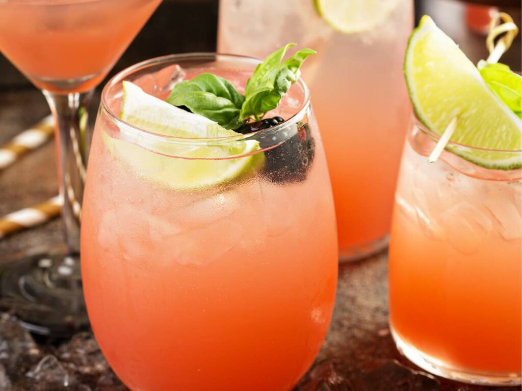 Three pink drinks with lime and blackberry garnishes.