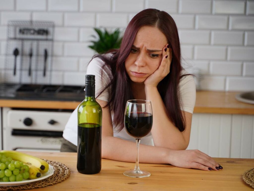 A woman is sitting at the kitchen table with a glass of wine.