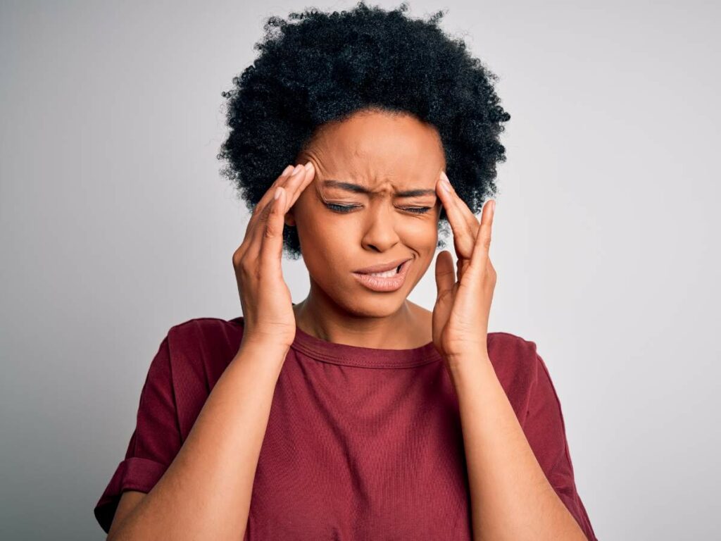 A woman with a headache is holding her hands on her head.