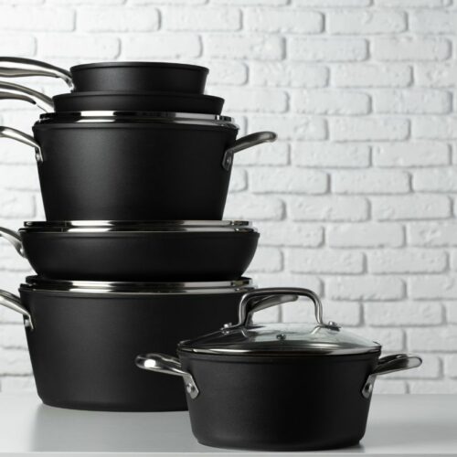 A stack of black cookware with lids against a white brick background.