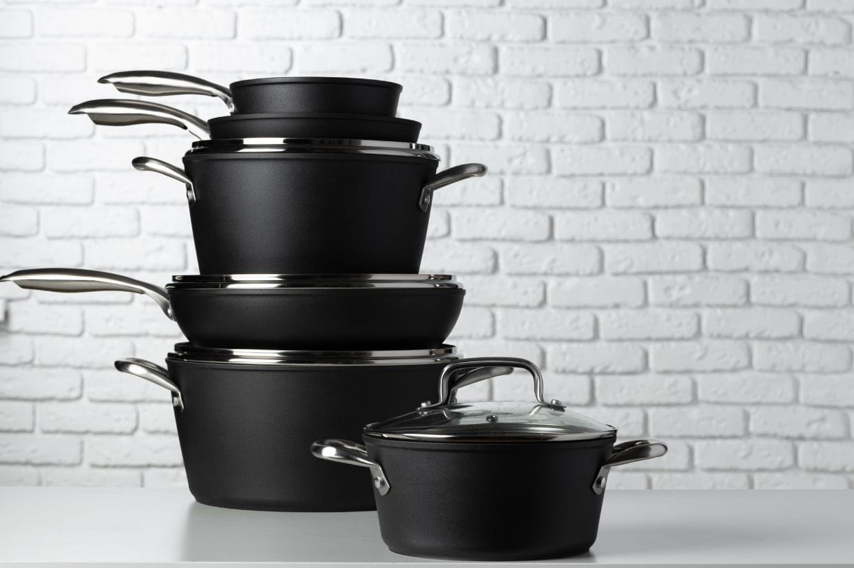 A stack of black cookware with lids against a white brick background.