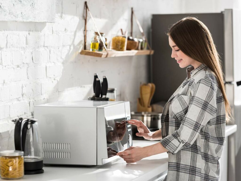 A woman using a microwave in a modern kitchen.