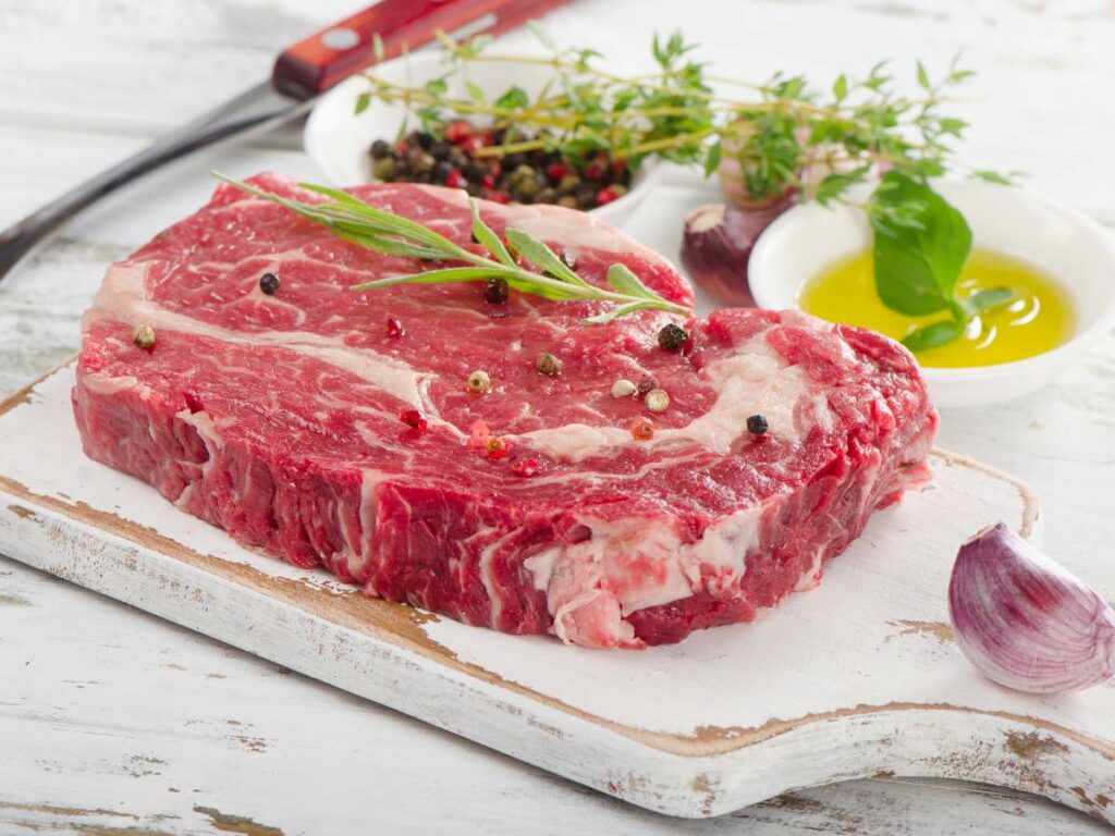 A ribeye steak on a cutting board with herbs and spices.