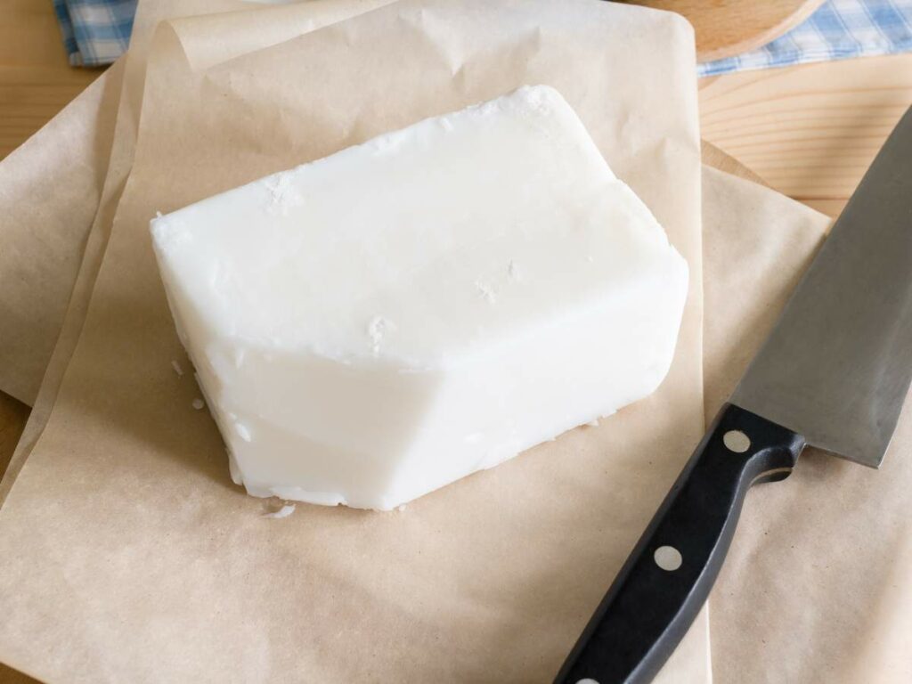 A block of beef tallow on parchment paper next to a kitchen knife.