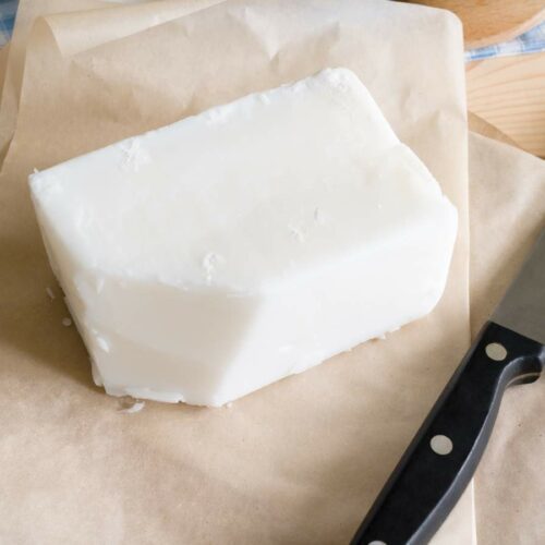 A block of beef tallow on parchment paper next to a kitchen knife.