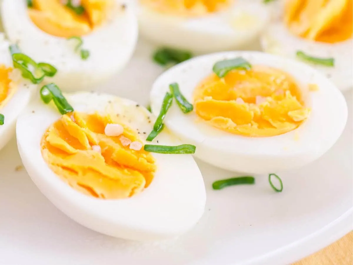 Halved hard-boiled eggs garnished with chives on a white plate.
