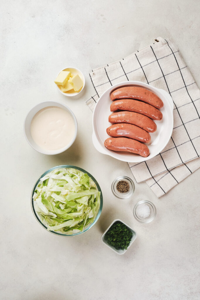 Sausages on a plate, bowls of shredded cabbage, seasonings, sauce, and butter.
