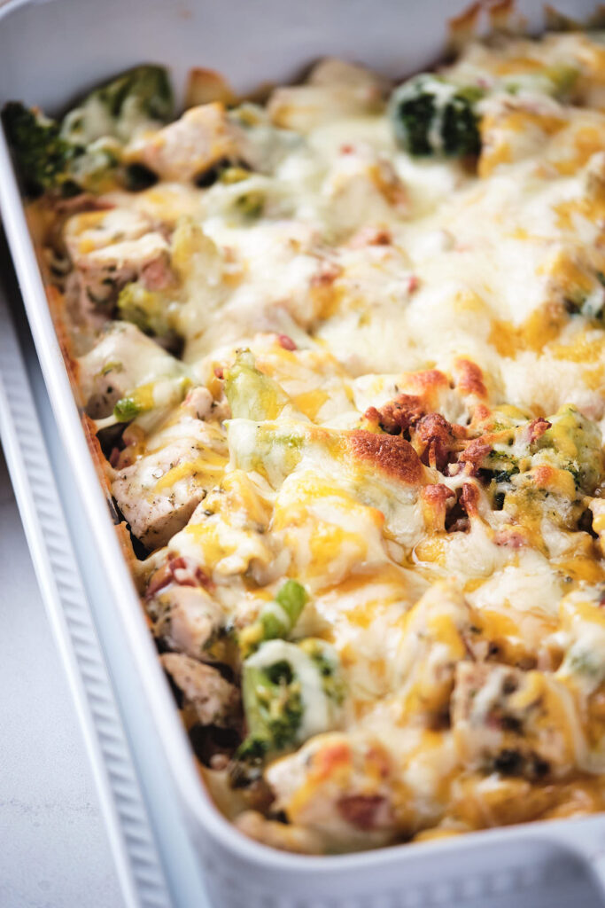 A close-up of a cheesy chicken bacon ranch casserole in a white baking dish.