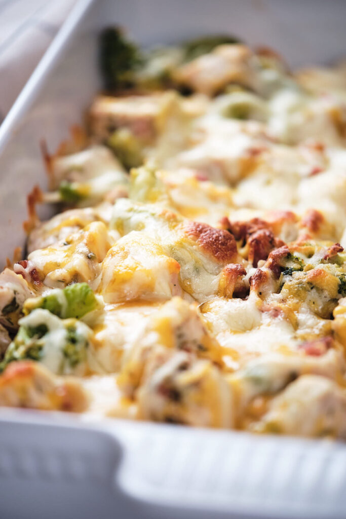 Baked chicken and broccoli casserole topped with melted cheese in a white baking dish.