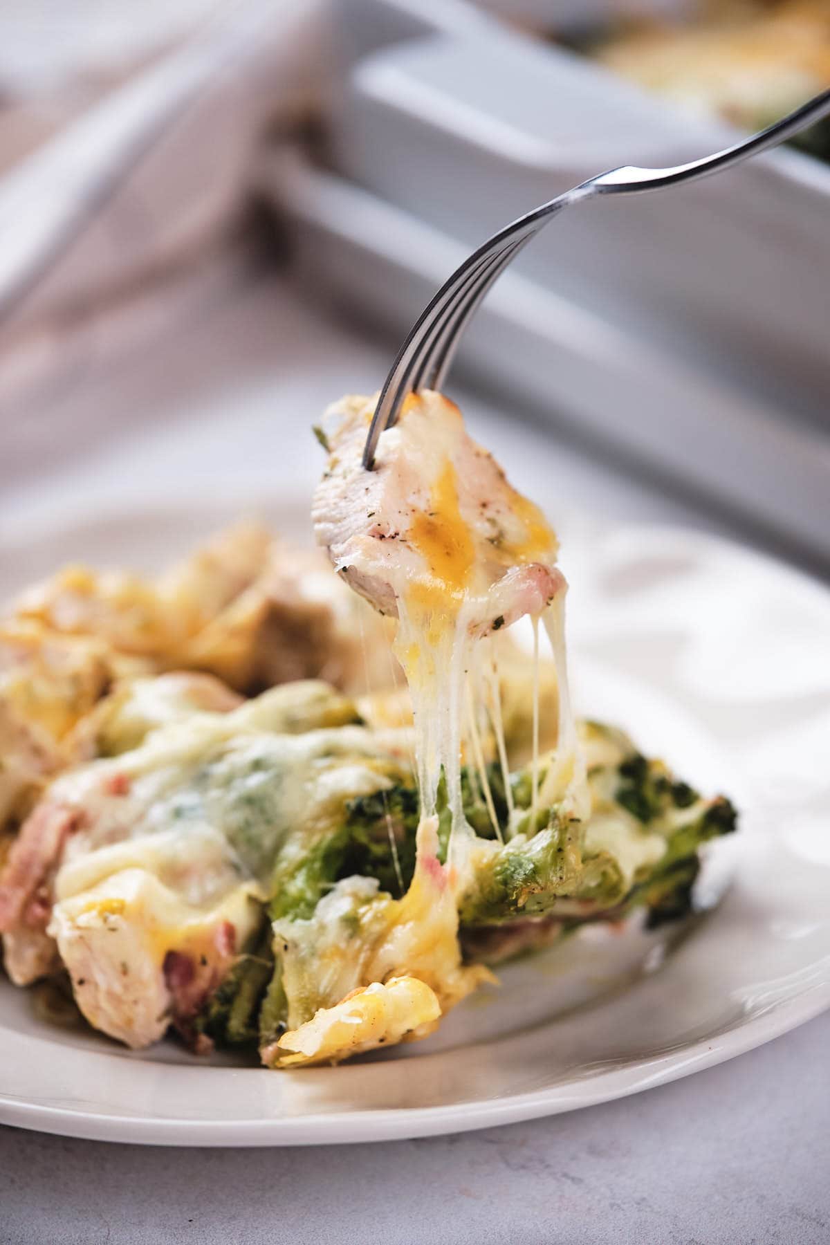 A fork lifting a cheesy bite of broccoli and chicken casserole from a plate.