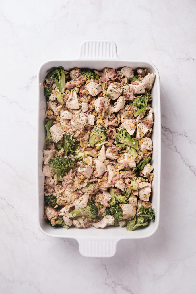 Chicken and broccoli casserole in a white rectangular baking dish on a marble surface.