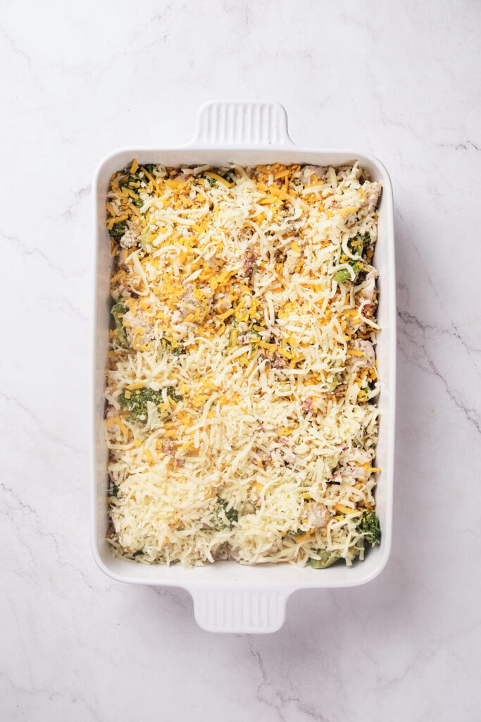 A casserole dish with uncooked cheese on top on a marble countertop.