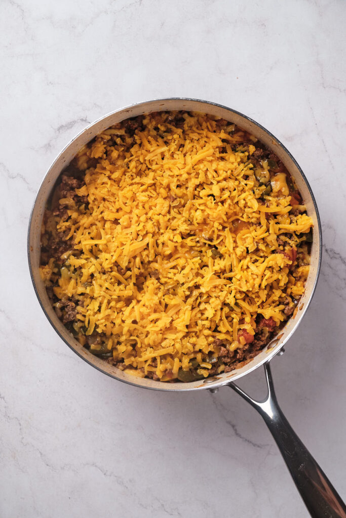 A skillet filled with seasoned ground beef, topped with a layer of shredded cheddar cheese.