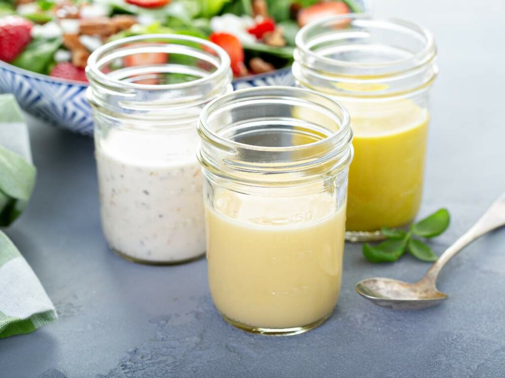 Three jars of homemade salad dressings with a spoon alongside.