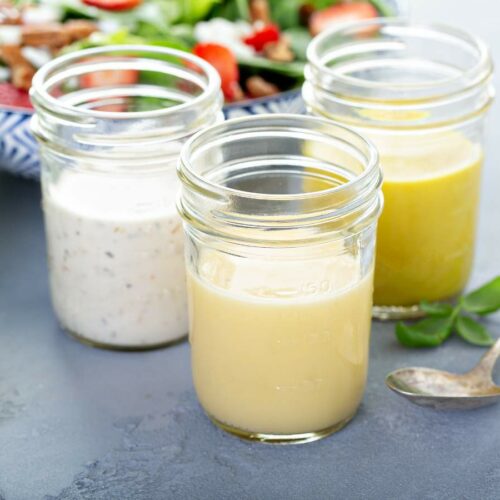 Three jars of homemade salad dressings with a spoon alongside.