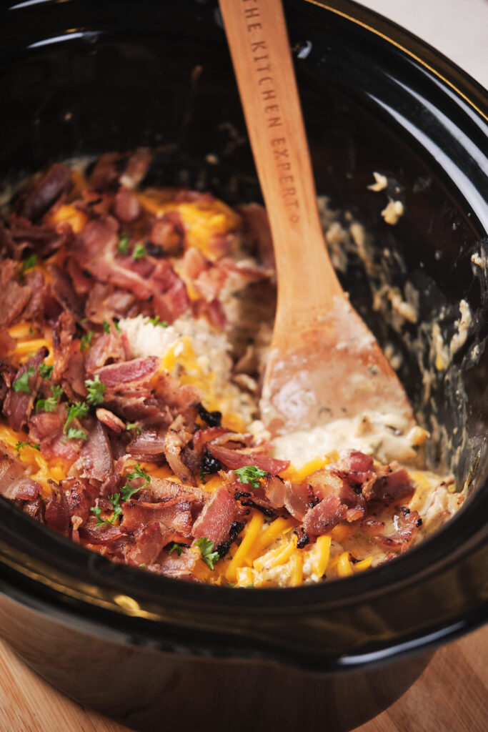 Black pot containing a creamy bacon and cheese, with a wooden spoon.