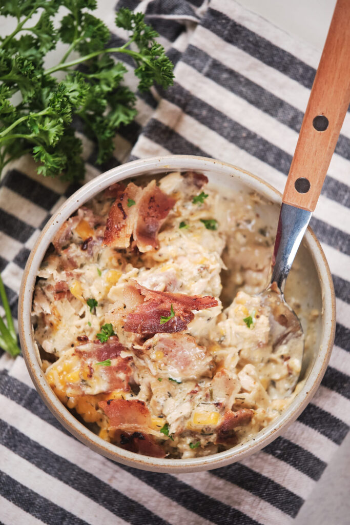 A bowl of slow cooker crack chicken garnished with parsley on a striped cloth.