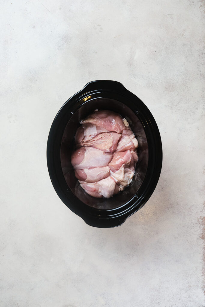 Raw chicken breast in a black slow cooker on a grey countertop.