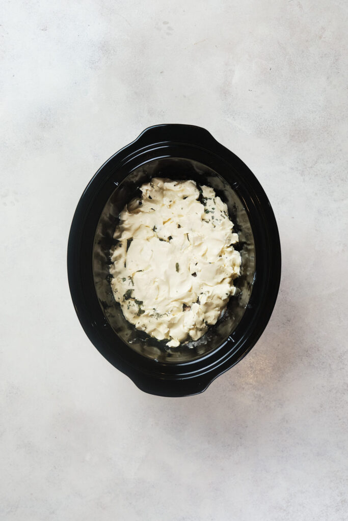 Cream cheese over chicken in a black crock pot.
