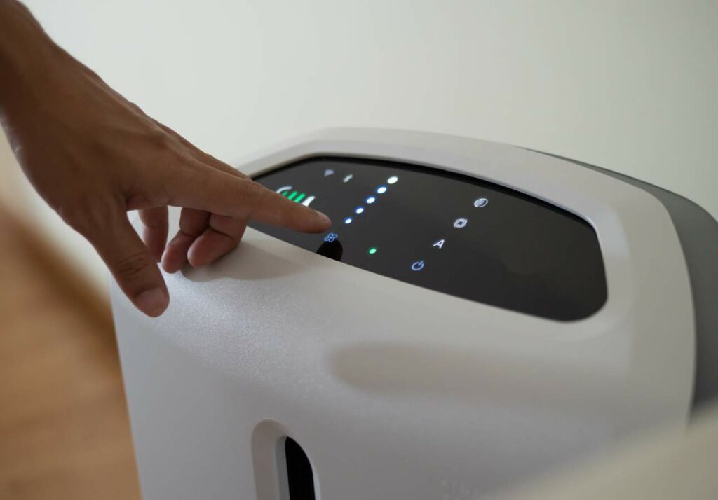 A person's hand adjusting settings on the touch screen of a modern, white electronic device with indicator lights.