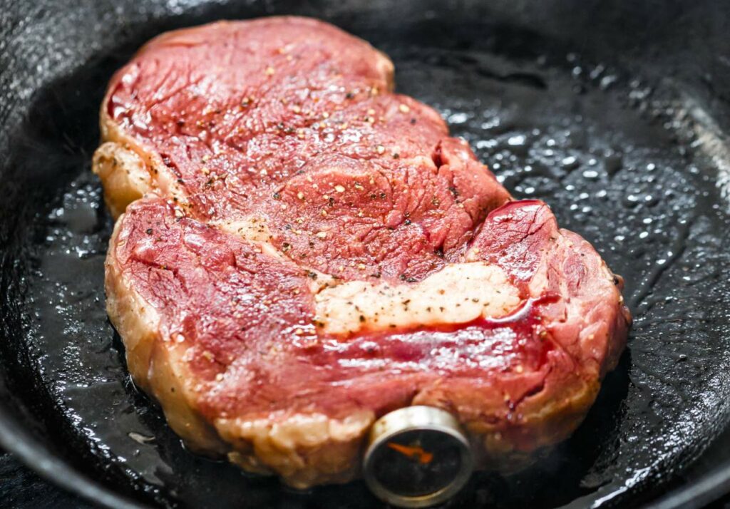 A seasoned steak cooking in a black cast iron skillet.