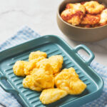 Six pieces of cooked cheese curds are arranged on a blue tray with handles.