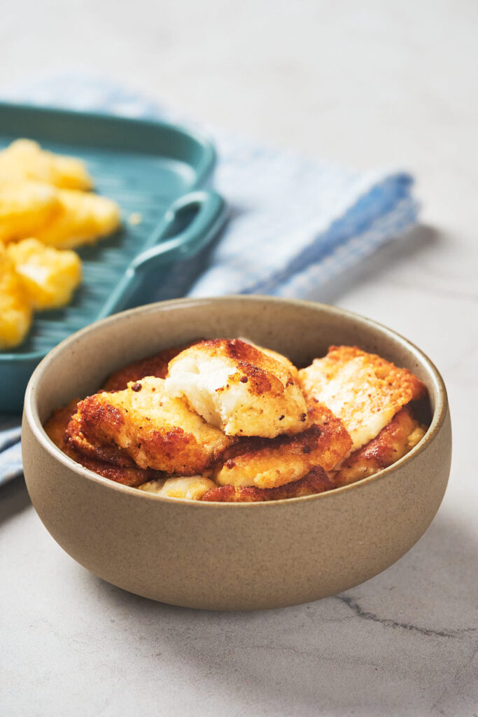 A bowl of crispy, golden-brown fried food, with a green dish containing more pieces.