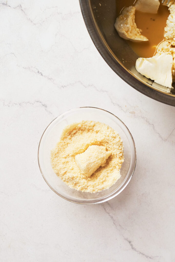 A small glass bowl filled with grated cheese sits on a marble countertop.