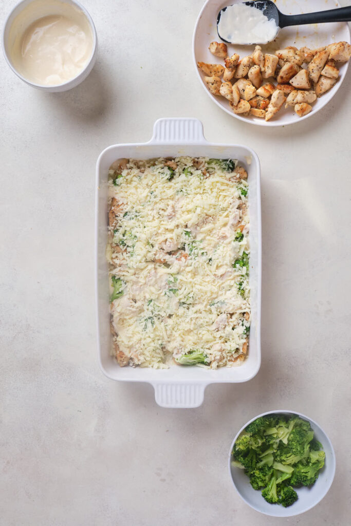 A white rectangular baking dish filled with uncooked chicken broccoli alfredo casserole.