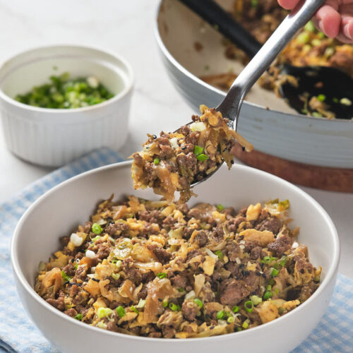 A person holding a spoonful of a dish with minced meat, scrambled eggs, and chopped green onions.