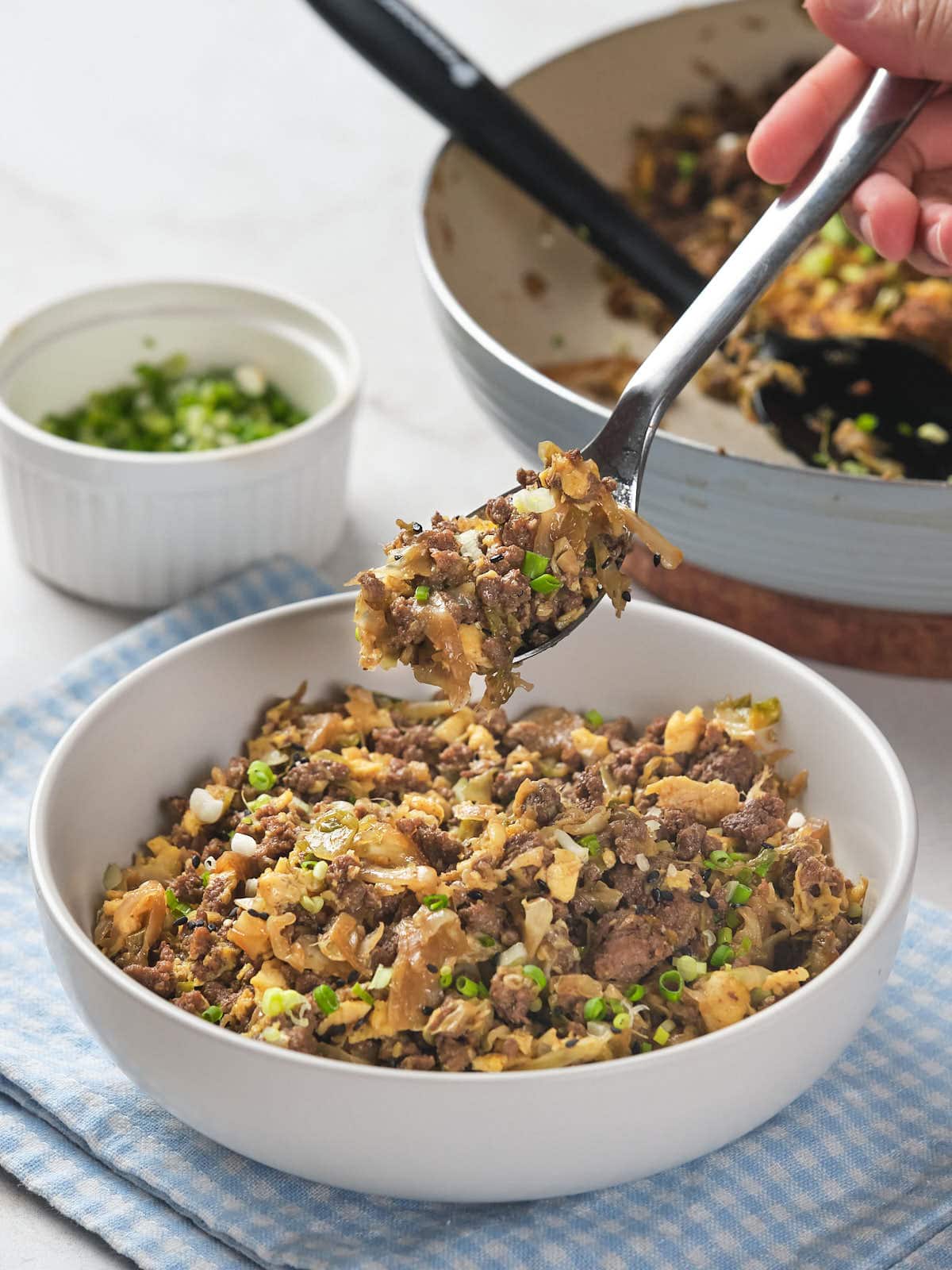 A person holding a spoonful of a dish with minced meat, scrambled eggs, and chopped green onions.