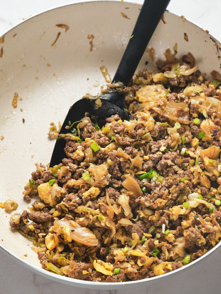 Egg roll in a bowl being stirred with a black spatula.