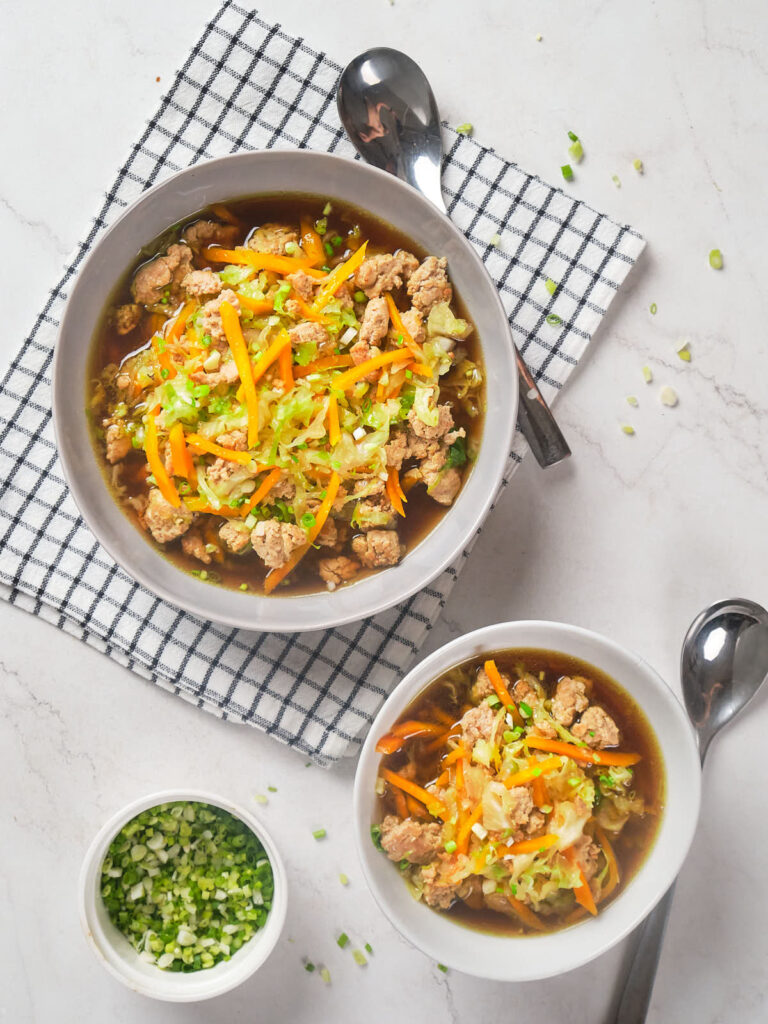 Two bowls of soup containing vegetables and minced meat,.
