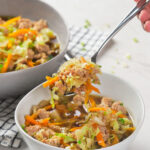 A hand holding a spoonful of a mixed vegetable and meat dish over a white bowl.