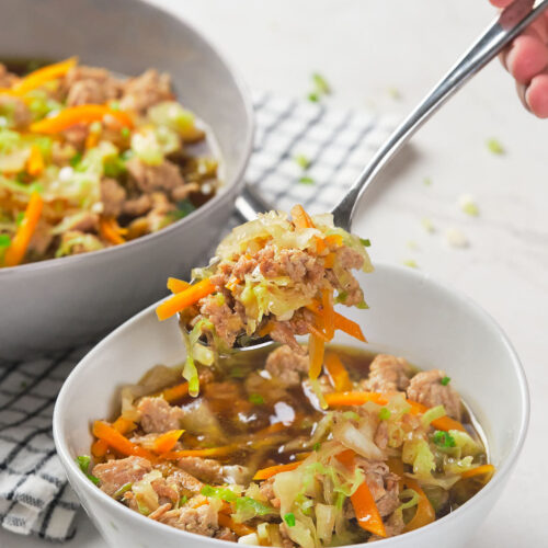 A hand holding a spoonful of a mixed vegetable and meat dish over a white bowl.