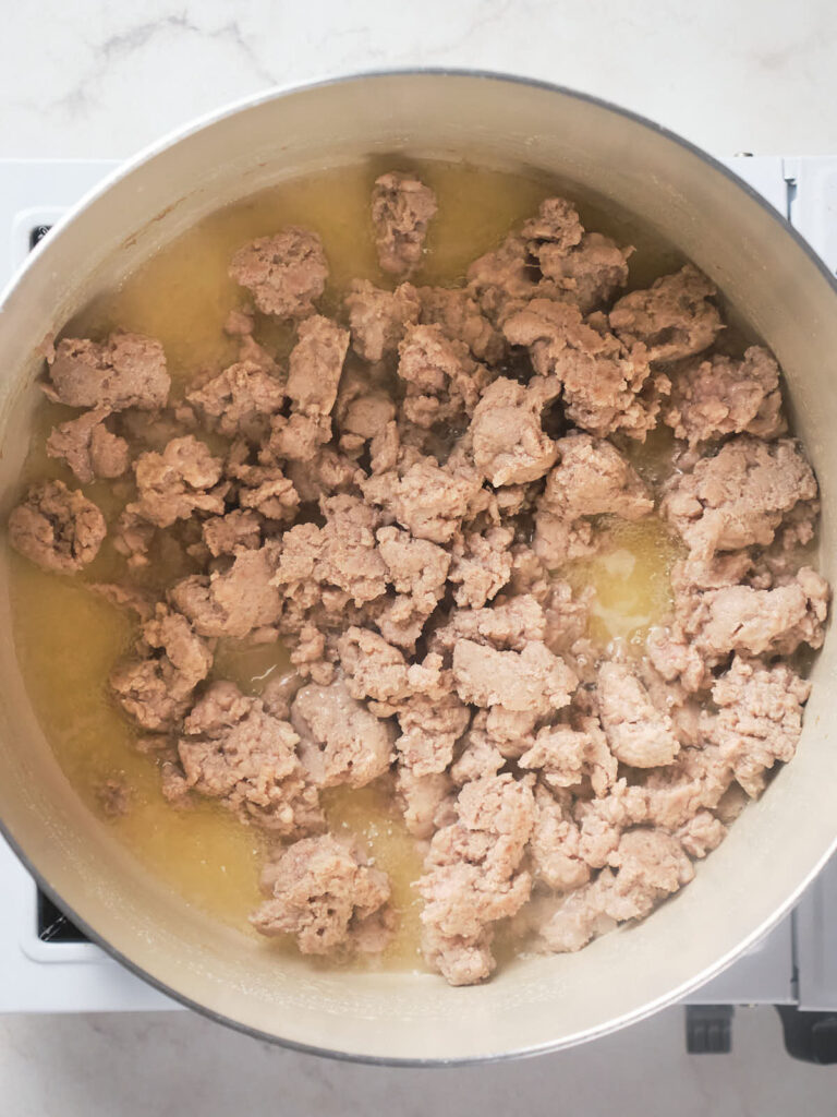 Meat being cooked in a large stainless steel pot on a stove.