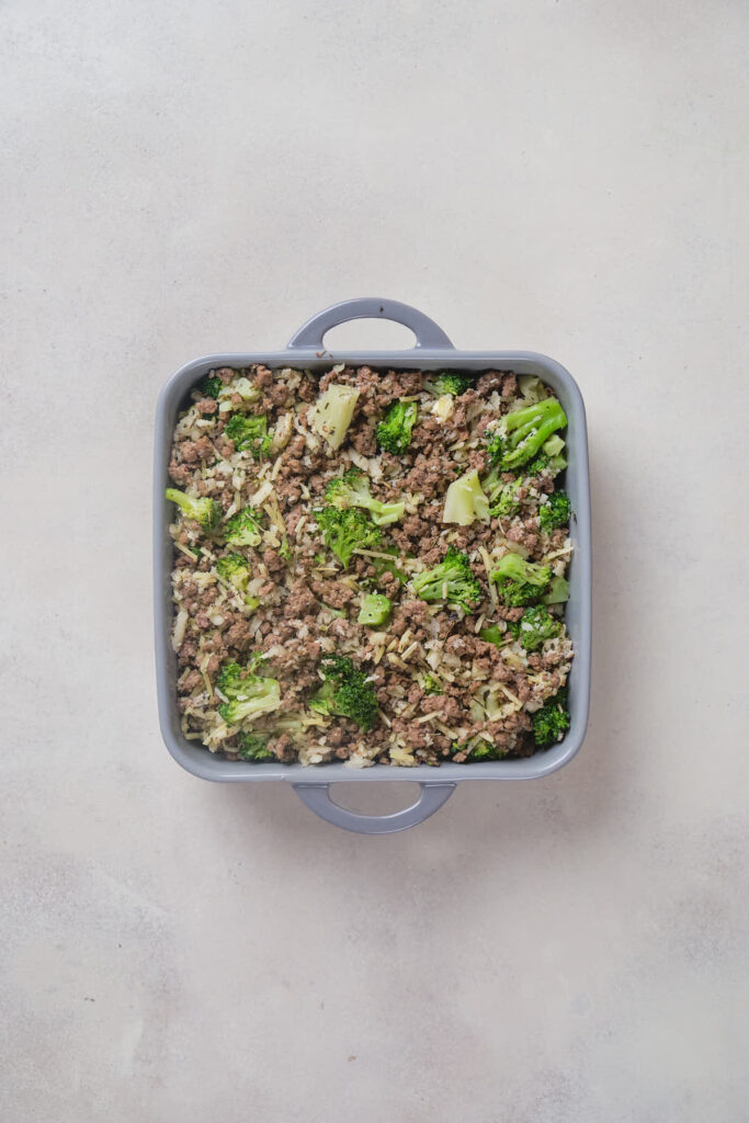 A square baking dish containing ground beef and broccoli casserole on a light-colored surface.