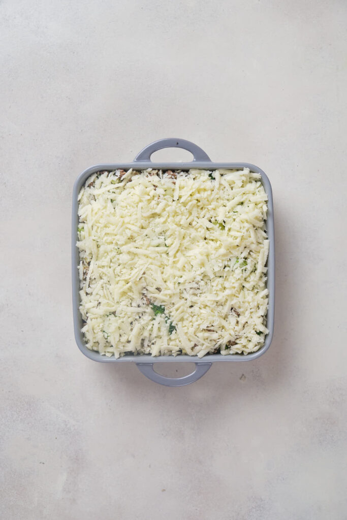 A square baking dish filled with uncooked ground beef and broccoli casserole.