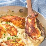 A skillet with creamy garlic chicken being stirred by a wooden spoon.