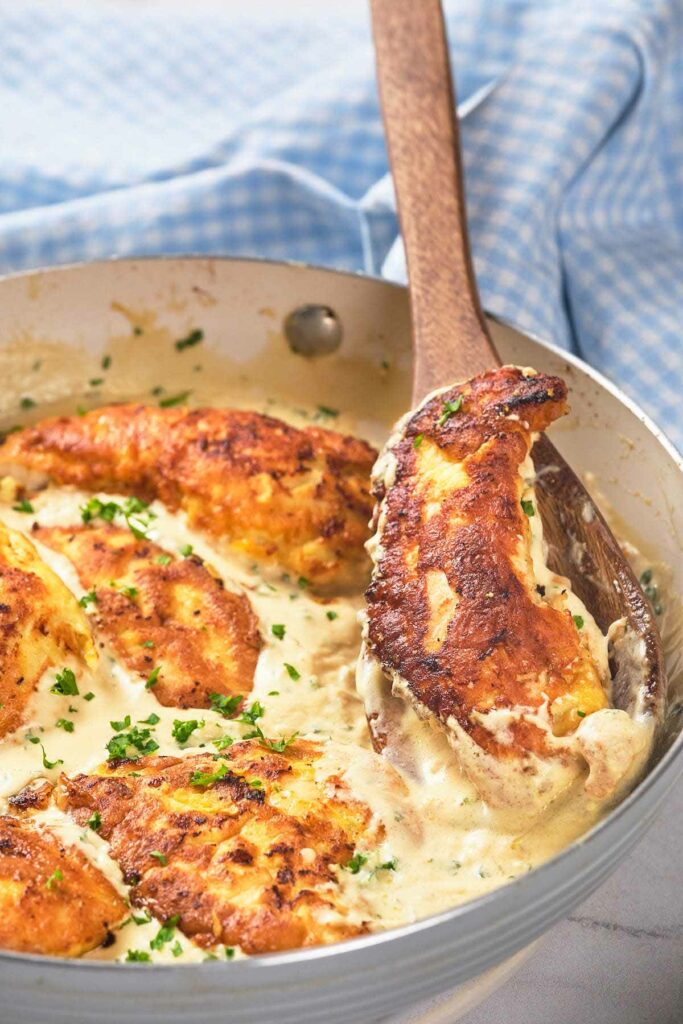 A skillet with creamy garlic chicken being stirred by a wooden spoon.
