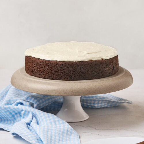 A chocolate cake with white frosting is displayed on a cake stand.