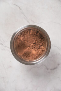 A metal bowl filled with chocolate powder on a white marble surface.