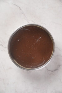 A round metal container filled with a smooth, dark chocolate mixture, placed on a light gray marble surface.