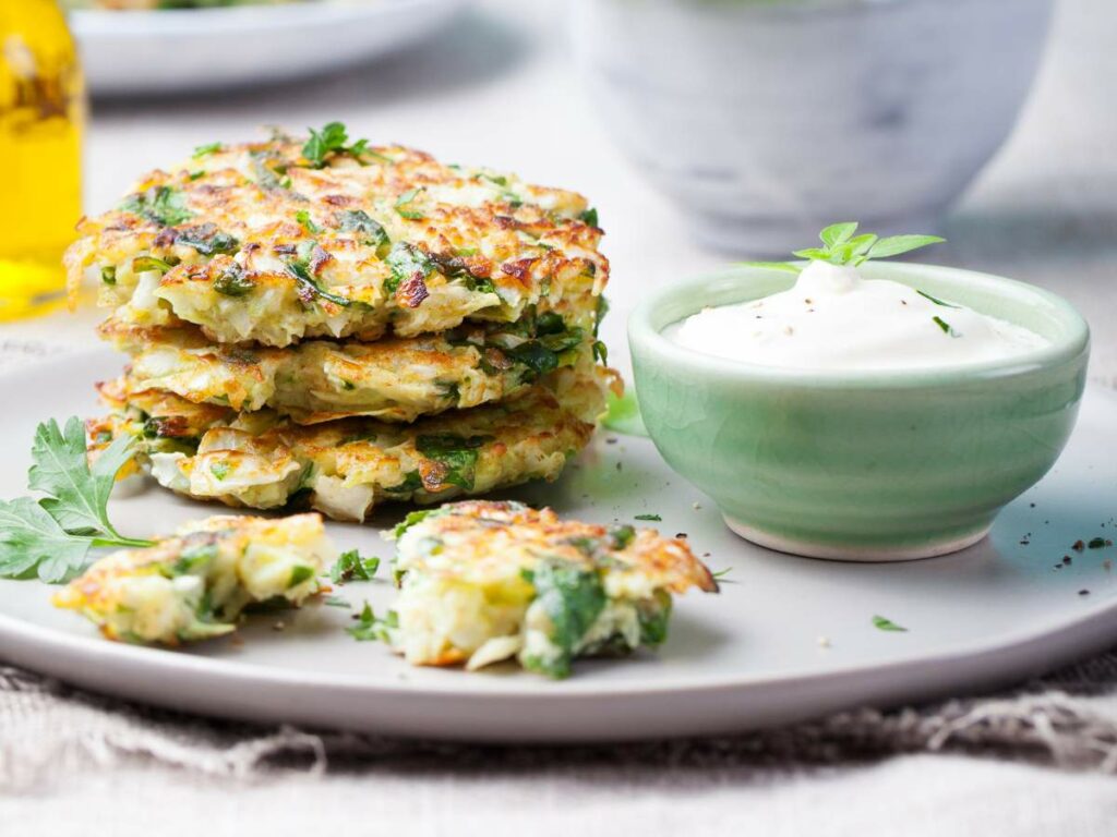 A plate with vegetable fritters accompanied by a bowl of white dipping sauce.