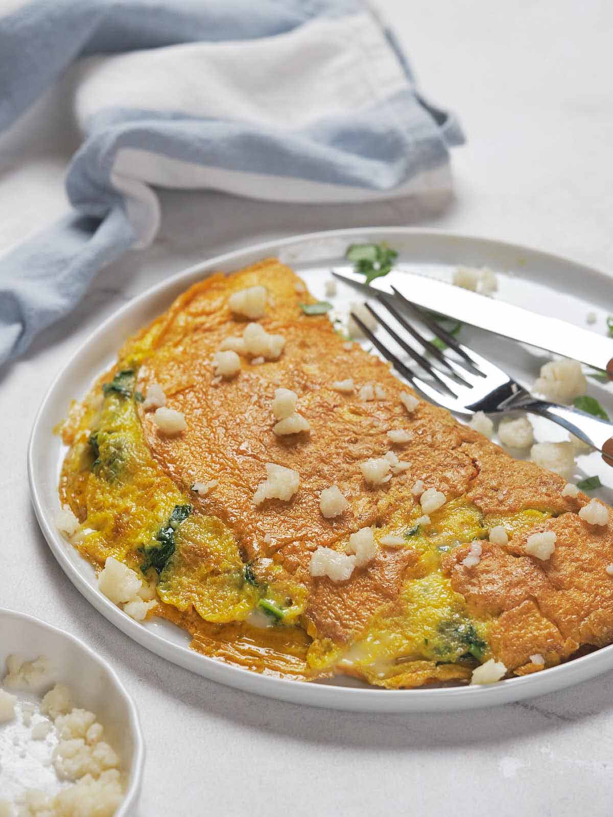 A plated omelette garnished with cheese crumbles, accompanied by a fork and knife.